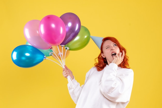 Front view of young woman holding cute colorful balloons on yellow wall