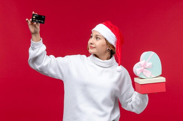 Front view young woman holding gifts and bank card on a red background