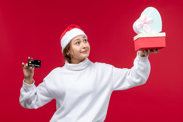 Front view young woman holding gifts and bank card on red background