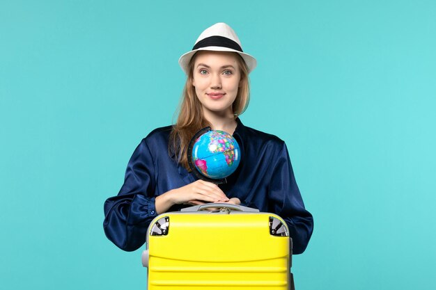 Вид спереди молодая женщина, держащая глобус и готовящаяся к отпуску на синем фоне самолета, женский отпуск, путешествие, путешествие на море