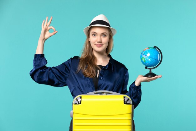 Front view young woman holding globe and preparing for vacation on blue floor plane female vacation journey voyage sea