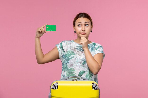 Front view young woman holding green bank card on vacation thinking on pink wall voyage vacation trip summer rest woman