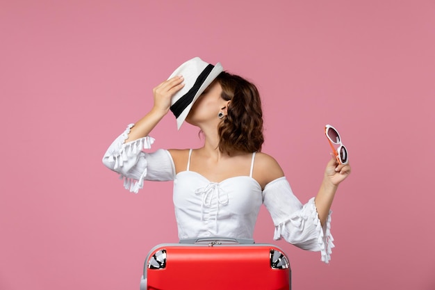 Foto gratuita vista frontale della giovane donna che tiene cappello e occhiali da sole con borsa rossa sul muro rosa