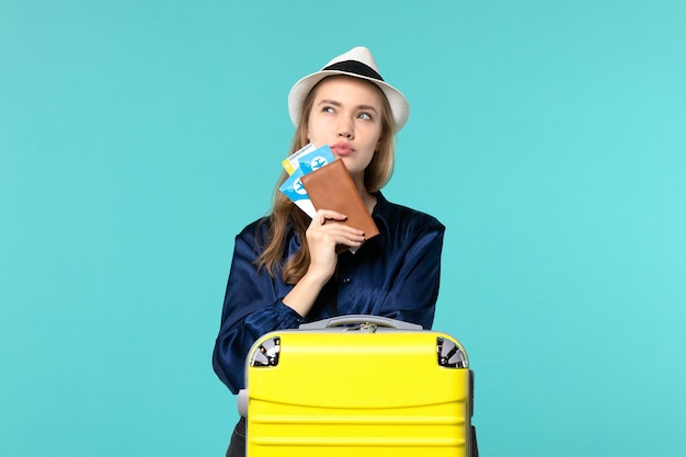 Вид спереди молодая женщина, держащая билеты и готовящаяся к поездке, думает на синем фоне, путешествие на самолете, море, отдых, путешествие, путешествие