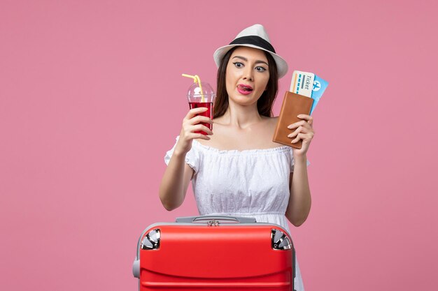 Front view young woman holding juice and tickets on vacation on a pink wall summer rest voyage woman trip