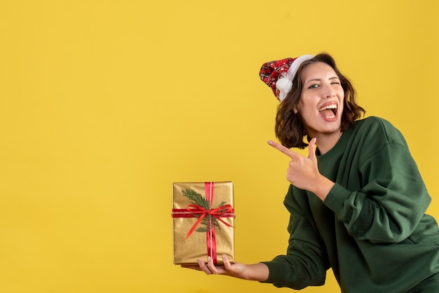 Front view of young woman holding little christmas present on a yellow wall