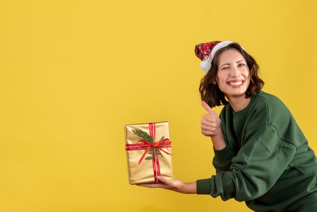 노란색 벽에 작은 크리스마스 선물을 들고 젊은 여자의 전면보기
