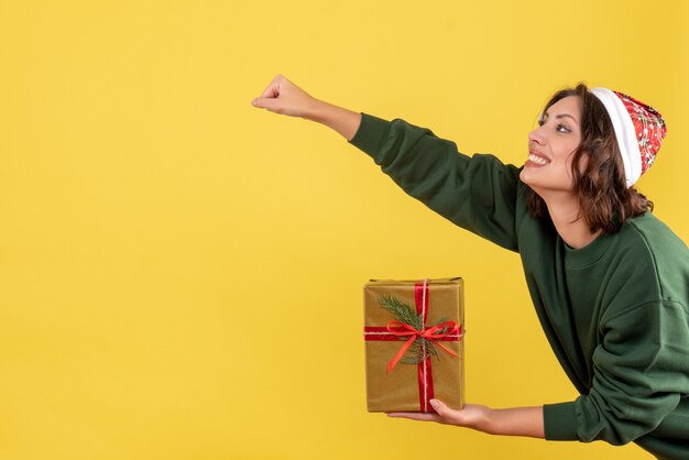 Вид спереди молодой женщины, держащей маленький рождественский подарок на желтой стене