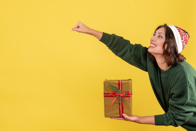 黄色の壁に小さなクリスマスプレゼントを保持している若い女性の正面図
