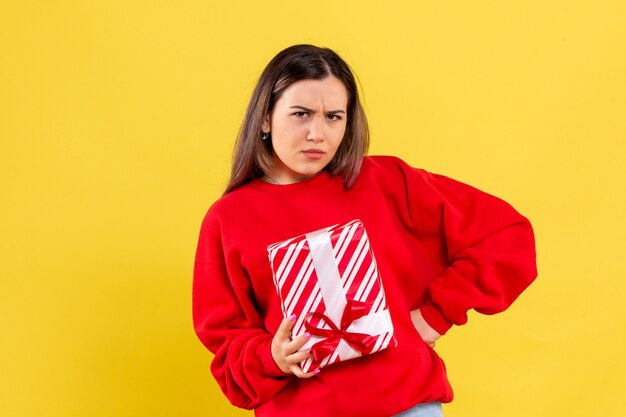 Front view of young woman holding little gift on a yellow wall