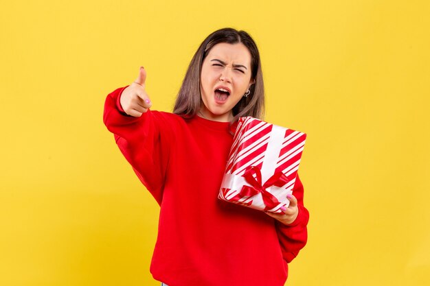 Front view of young woman holding little gift on the yellow wall