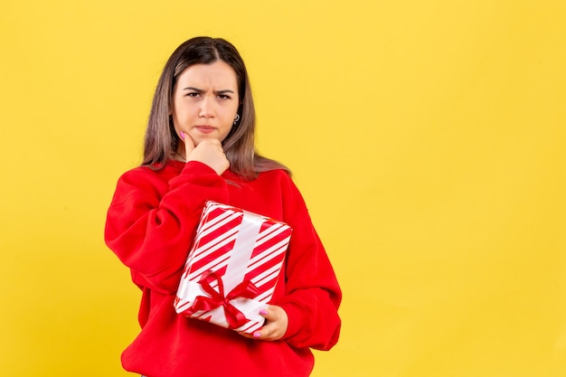 Front view of young woman holding little gift on yellow wall