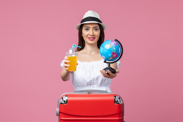 Front view young woman holding little globe and cocktail on a pink wall summer voyage trip heat color vacation