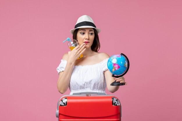 Front view young woman holding little globe and cocktail on pink wall trip voyage heat color vacation summer