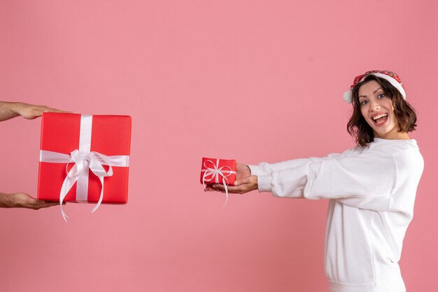 Front view of young woman holding little present and accepting gift from man on pink wall