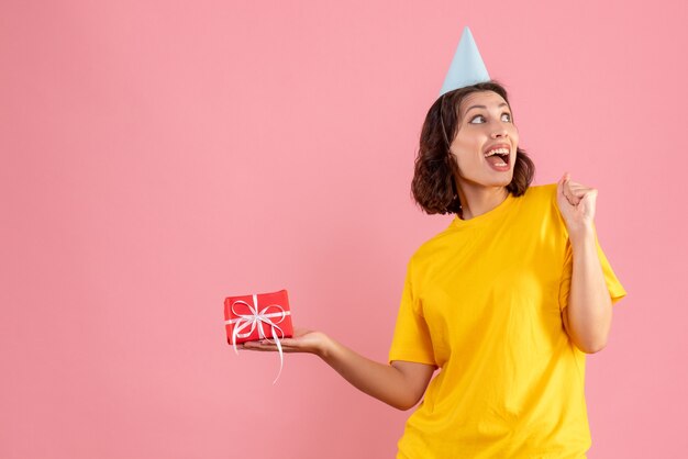 Front view of young woman holding little present on a pink wall