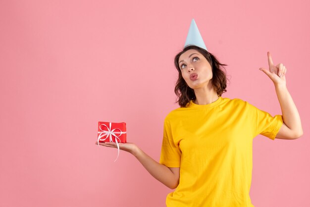 Front view of young woman holding little present on a pink wall