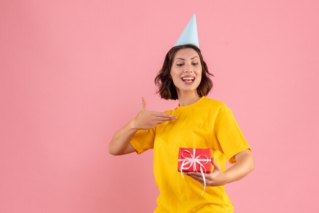 Front view of young woman holding little present on pink wall