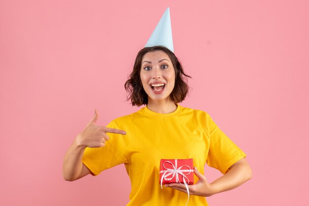ピンクの壁に小さなプレゼントを保持している若い女性の正面図