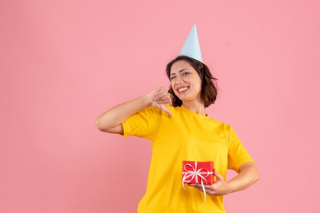 ピンクの壁に小さなプレゼントを保持している若い女性の正面図