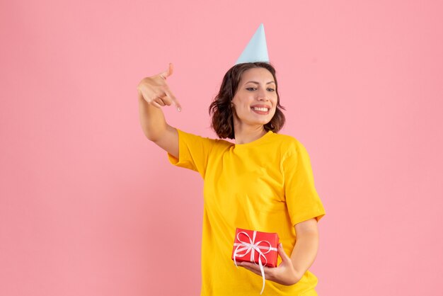 Front view of young woman holding little present on pink wall