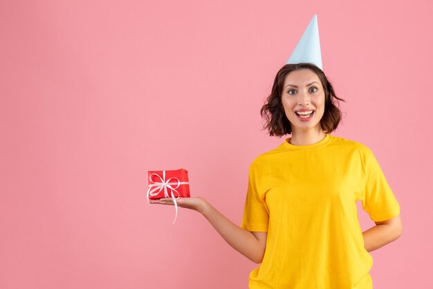 Front view of young woman holding little present on pink wall