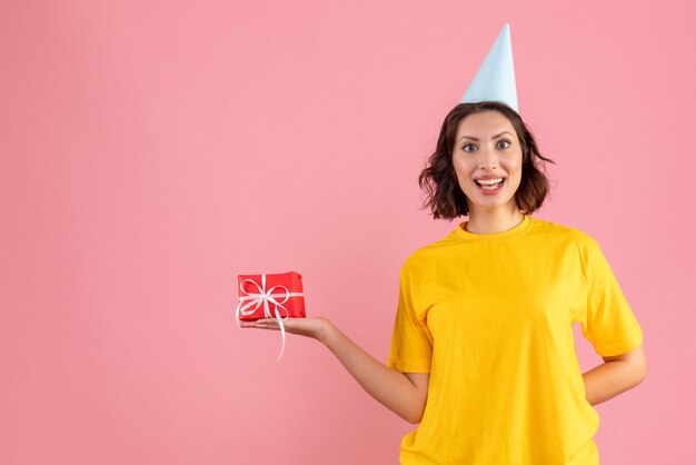 ピンクの壁に小さなプレゼントを保持している若い女性の正面図