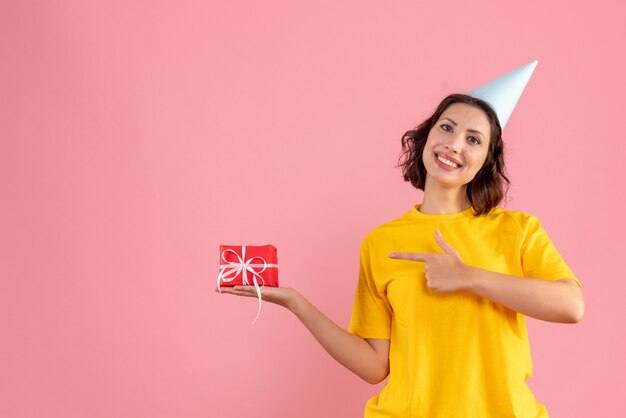 ピンクの壁に小さなプレゼントを保持している若い女性の正面図