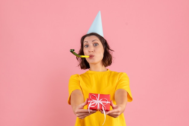 Front view of young woman holding little present on pink wall