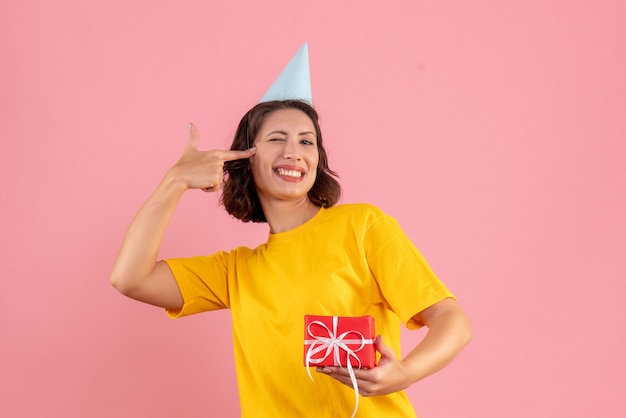 Front view of young woman holding little present on the pink wall