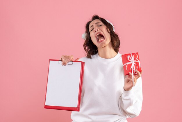 Front view of young woman holding little xmas present and file note on the pink wall