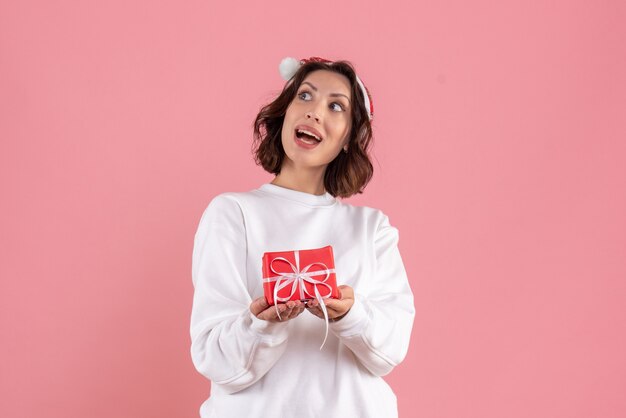 Вид спереди молодой женщины, держащей маленький рождественский подарок на розовой стене