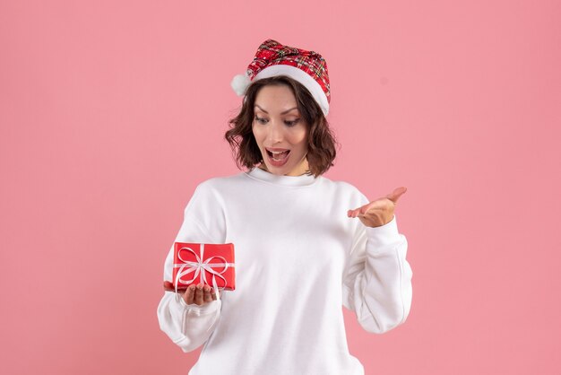 Front view of young woman holding little xmas present on pink wall