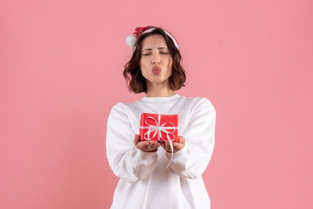 Front view of young woman holding little xmas present on pink wall