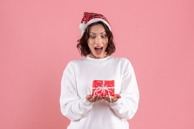 Front view of young woman holding little xmas present on pink wall