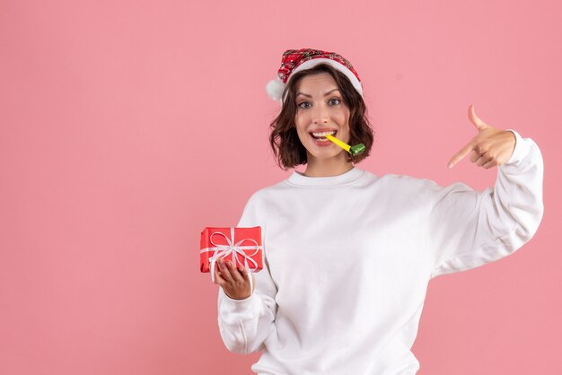 Front view of young woman holding little xmas present on pink wall