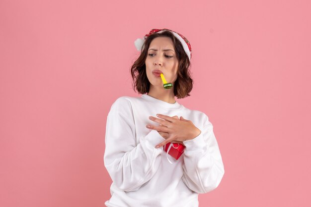 Front view of young woman holding little xmas present on pink wall