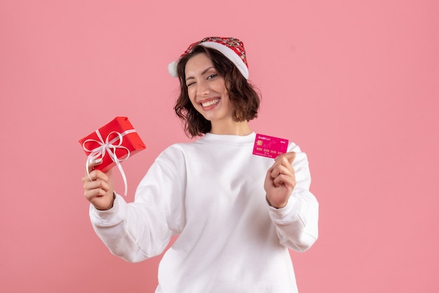 Front view of young woman holding little xmas present with bank card on pink wall