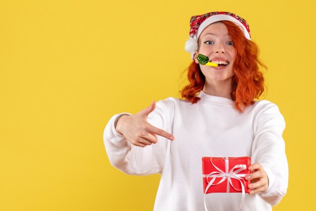 Front view of young woman holding little xmas present on a yellow wall