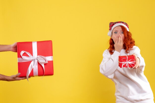 Front view of young woman holding little xmas present on yellow wall