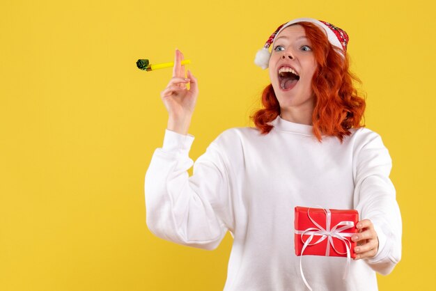 Front view of young woman holding little xmas present on yellow wall