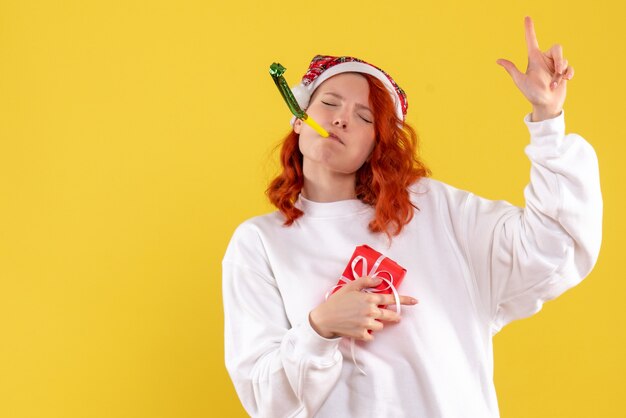 Front view of young woman holding little xmas present on yellow wall