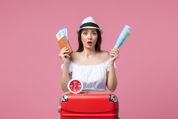 Front view young woman holding map and tickets on vacation on pink wall summer heat vacation trip woman voyage