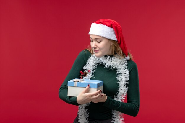 Front view young woman holding new year present on a red background