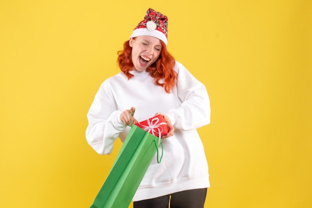 Front view of young woman holding package and little present on the yellow wall