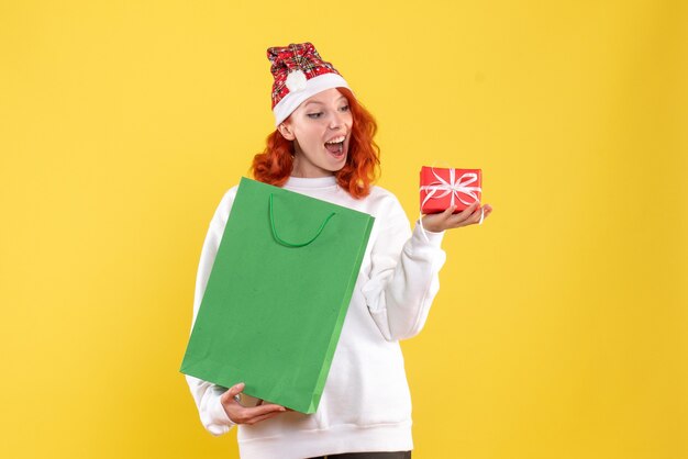 Front view of young woman holding package and little present on yellow wall