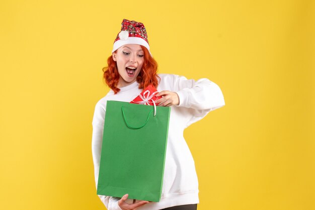 Front view of young woman holding package and little present on yellow wall