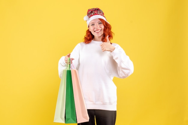 Front view of young woman holding packages from shopping on yellow wall