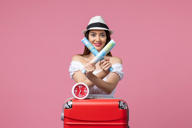 Front view young woman holding paper maps on vacation on a pink wall voyage trip summer heat woman vacation