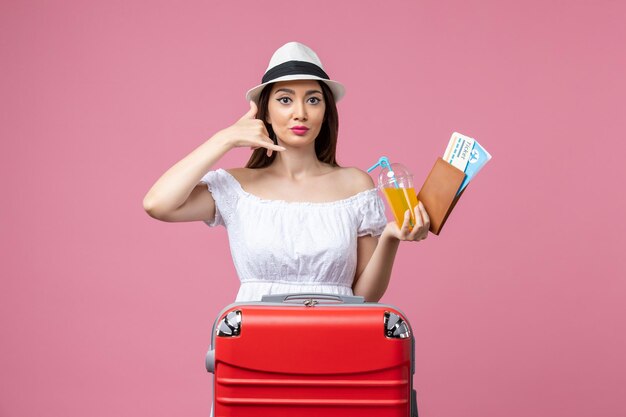 ピンクの壁の夏の旅行感情飛行機の航海で休暇とジュースの飛行機のチケットを保持している正面図若い女性